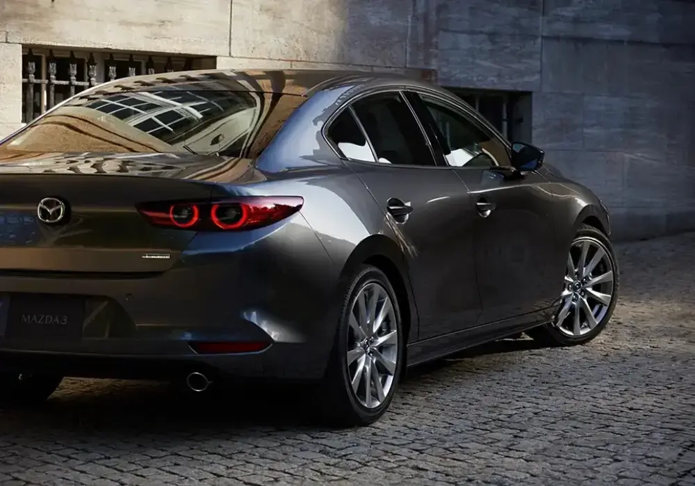 Parte trasera y lateral de un Mazda 3 sedán de color gris oscuro